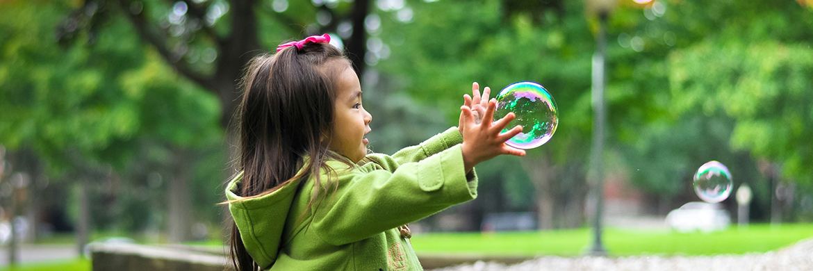 Smiling young girl reaching towards a bubble